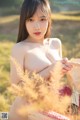 A naked asian woman holding a basket of wheat in a field.