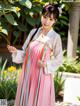 A woman in a pink and blue dress standing in a garden.