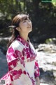 A woman in a pink and white kimono standing by a stream.