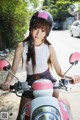 A woman wearing a helmet sitting on a pink motorcycle.