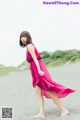 A woman in a pink dress walking on a beach.