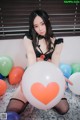 A woman sitting on a bed holding a bunch of balloons.