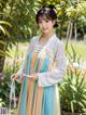 A woman in a blue and orange hanbok standing in a garden.