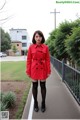 A woman in a red coat is standing on a sidewalk.