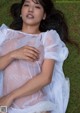 A woman laying on the grass in a sheer white dress.